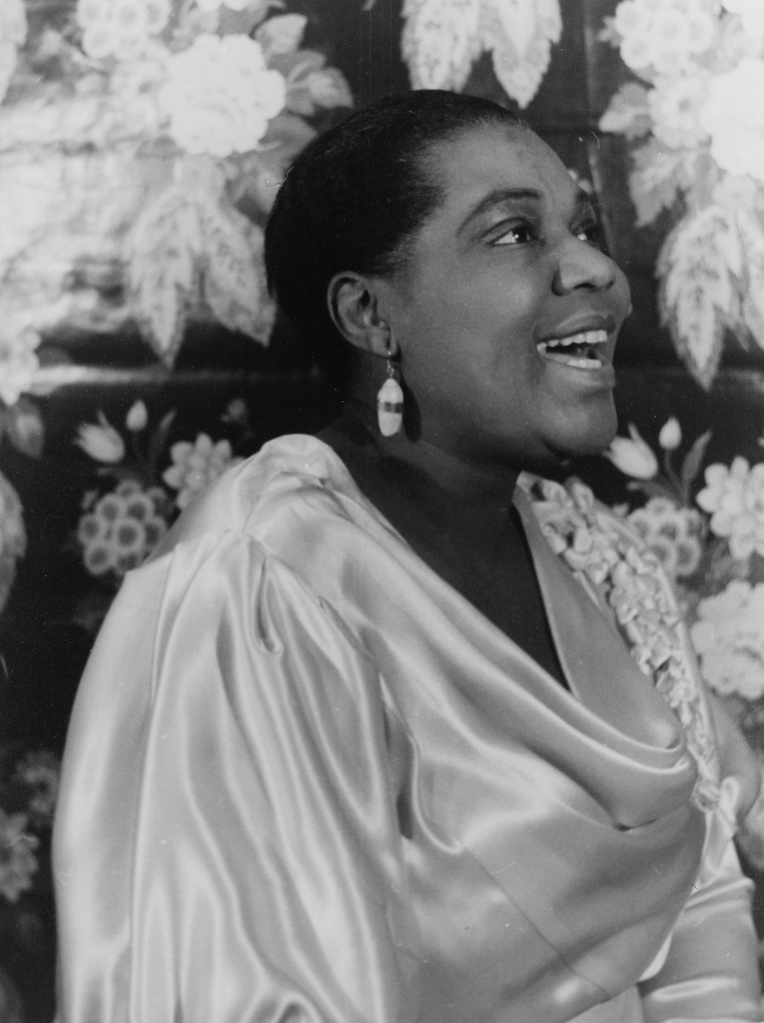 Close-up shot of Bessie Smith, either smiling or singing, facing right. She is wearing a white satin gown.