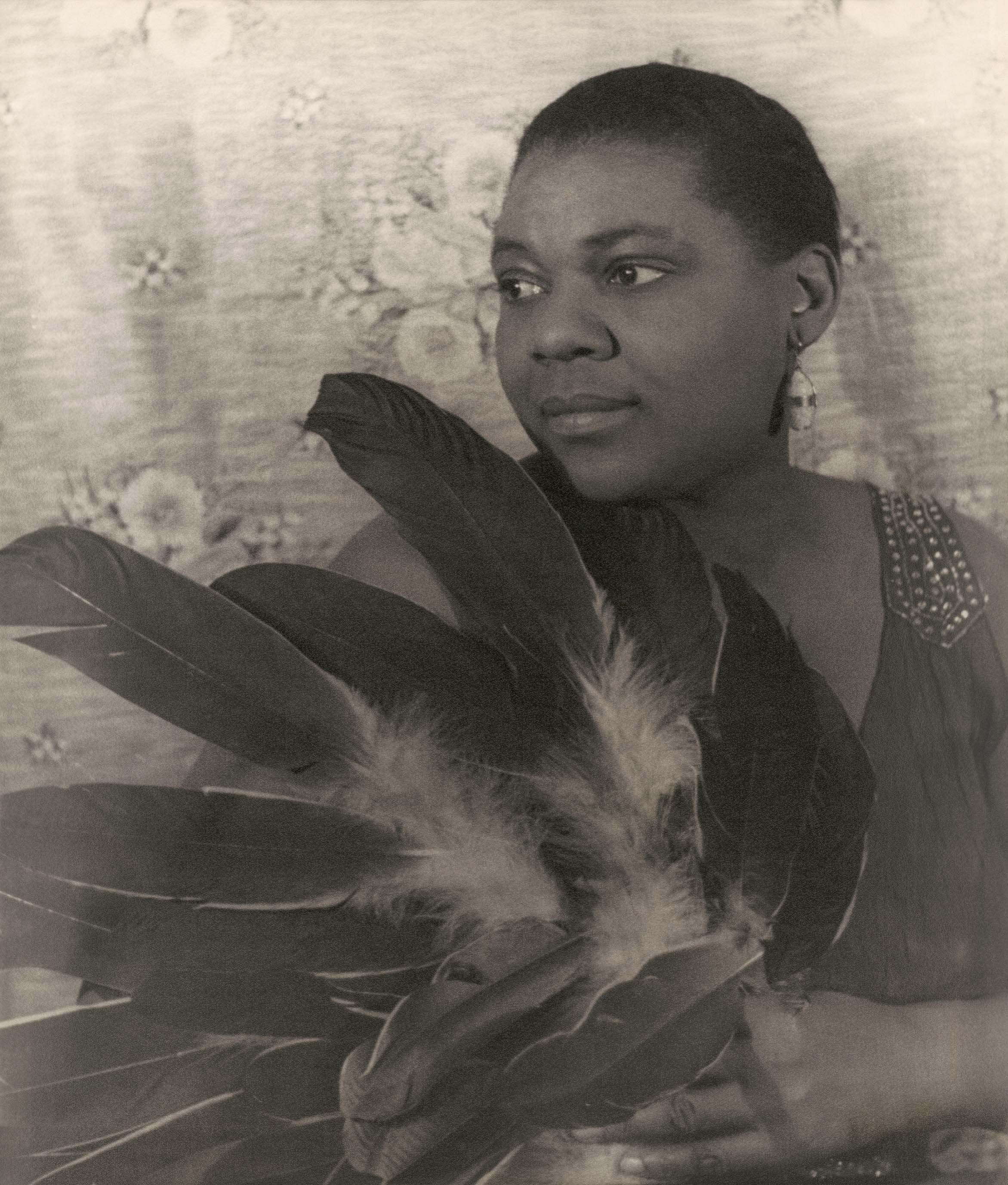 A 1936 Carl Van Vechten photograph of Bessie Smith sitting, holding feathers, facing left. This picture was likely taken at the same time as the previous one used here.