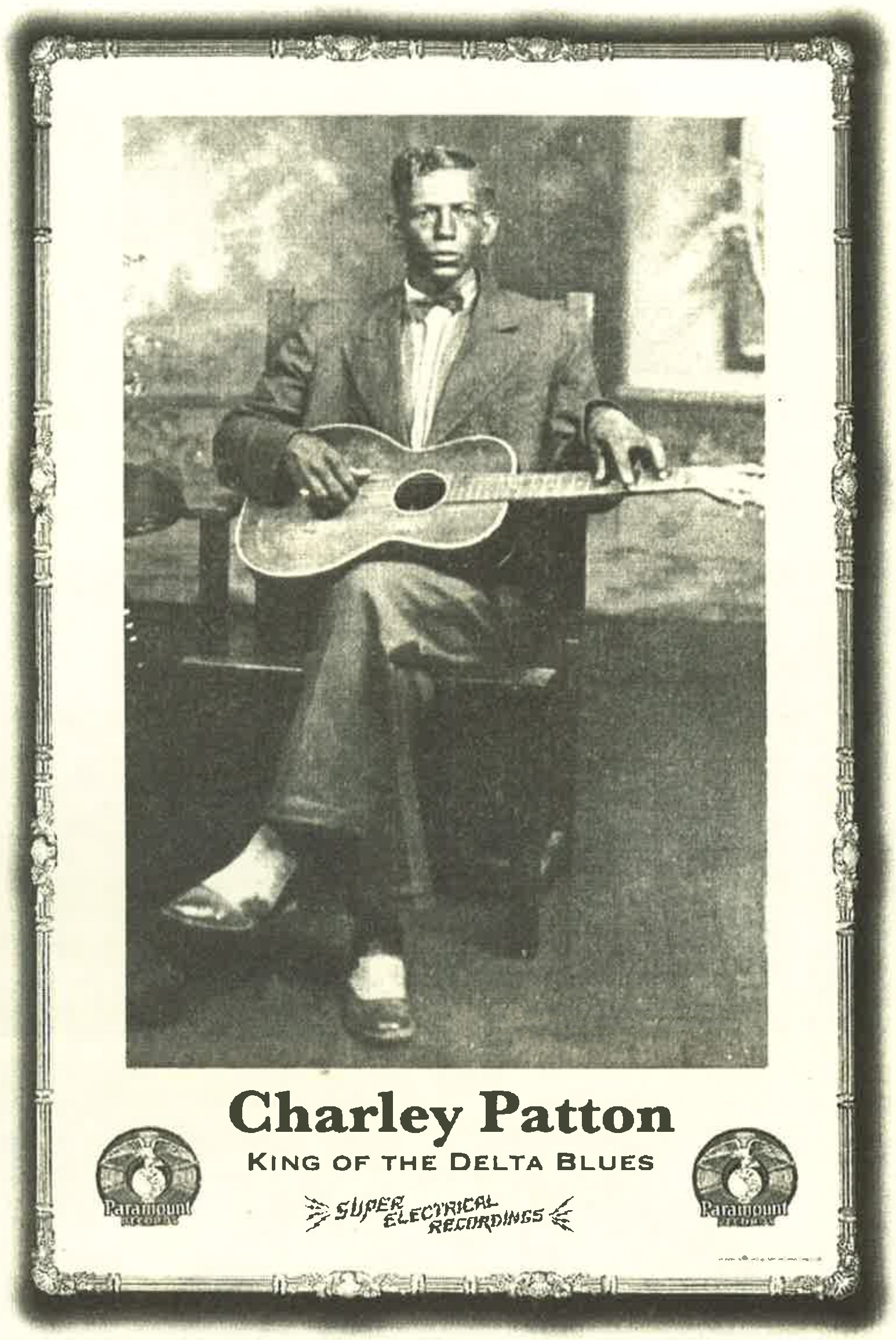Publicity photograph in black and white of blues musician Charley Patton. Here, he plays a guitar over his crossed legs while wearing a dress suit.